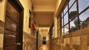 A hallway with a tiled floor, a doormat, a fire extinguisher, and a window with a view of trees. - Kasang Regency Hill Resort (Lansdowne)