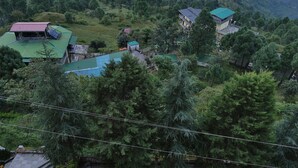 A mountainous landscape with a well-maintained garden featuring geometric hedges and a central seating area. - Kasang Regency Hill Resort (Lansdowne)