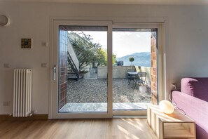 A room with a sliding glass door leading to an outdoor patio with a table and chairs, a radiator, and a purple sofa. - Casa sull'acqua (Varenna)