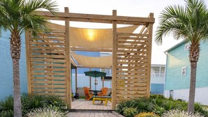 Une structure de pergola en bois avec un espace patio, des sièges d’extérieur et une pelouse bien entretenue.