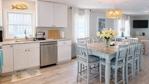 Une cuisine avec des meubles blancs, un lave-vaisselle en acier inoxydable, une table à manger en bois avec des chaises et un lustre.