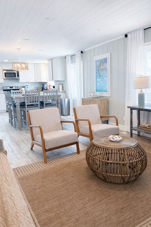 A modern living room with a dining area, a kitchen, and a large window with curtains.