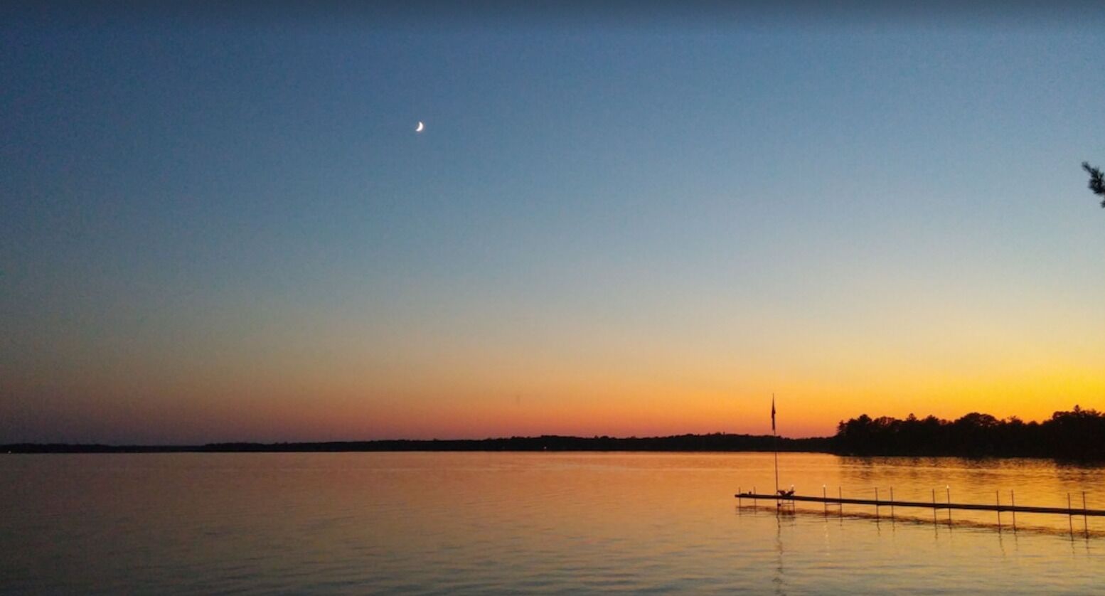 A calm lake at sunset with a dock extending into the water.