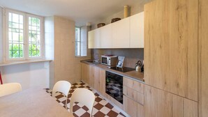 A compact kitchen with wooden cabinets, a microwave, and a dishwasher. There are two white chairs and a window providing natural light. - Villa Rachele (Varenna)