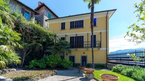 A two-story building with a yellow facade, a balcony, and a view of a body of water. - Villa Rachele (Varenna)