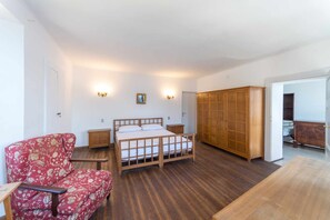 A bedroom with a wooden bed, a red floral armchair, a wooden wardrobe, and a wooden table.