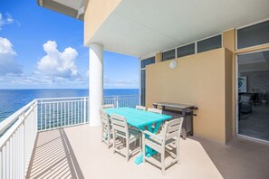 A balcony with a turquoise table and chairs, overlooking the ocean.