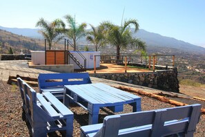 A patio area with blue wooden furniture, a stone wall, and a view of a mountainous landscape. - Casa Bejenado A - Casas Bejenado (El Paso)
