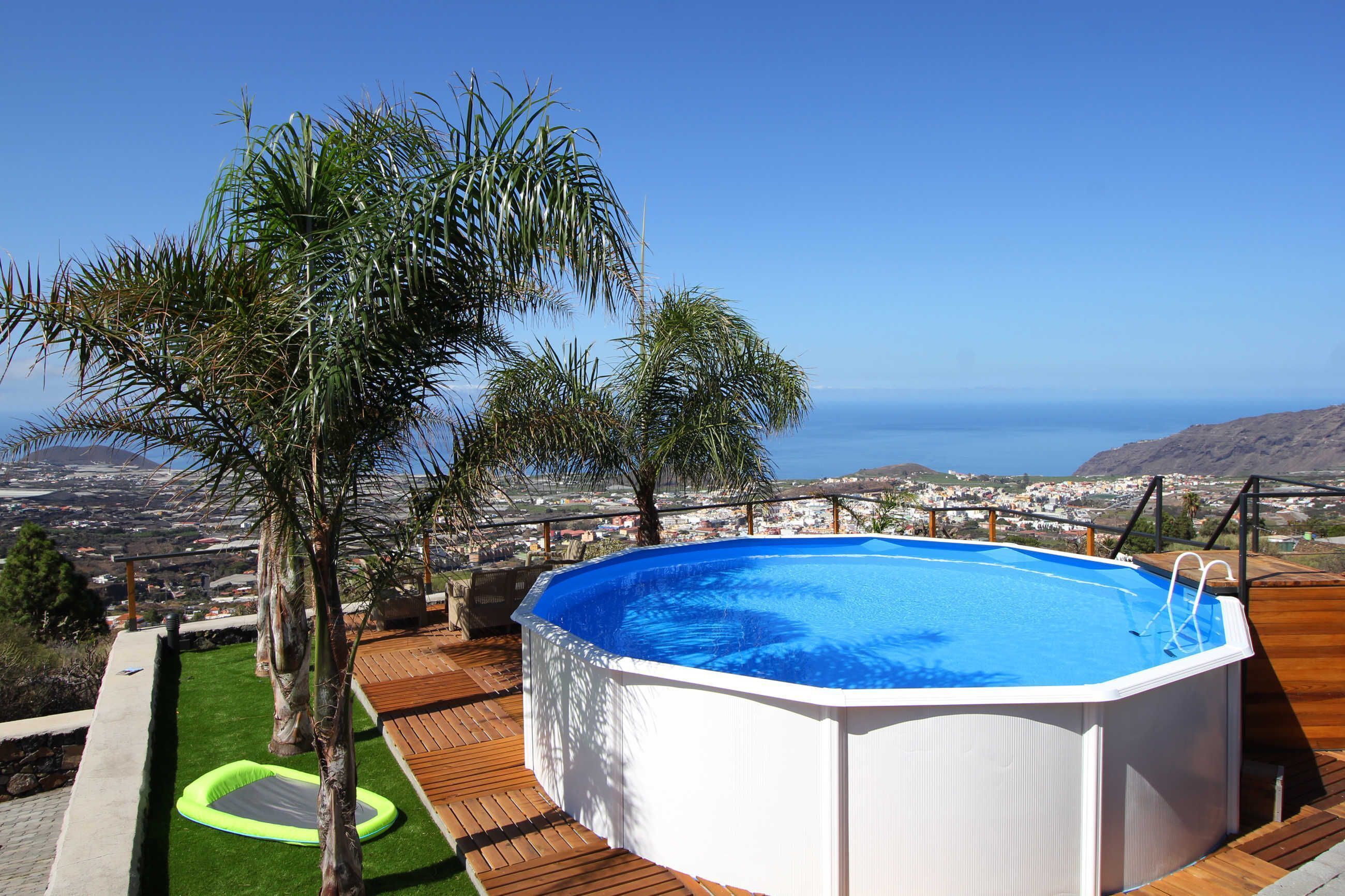 Ein Pool im Freien mit Holzterrasse, umgeben von Palmen, mit Blick auf eine Küstenstadt.