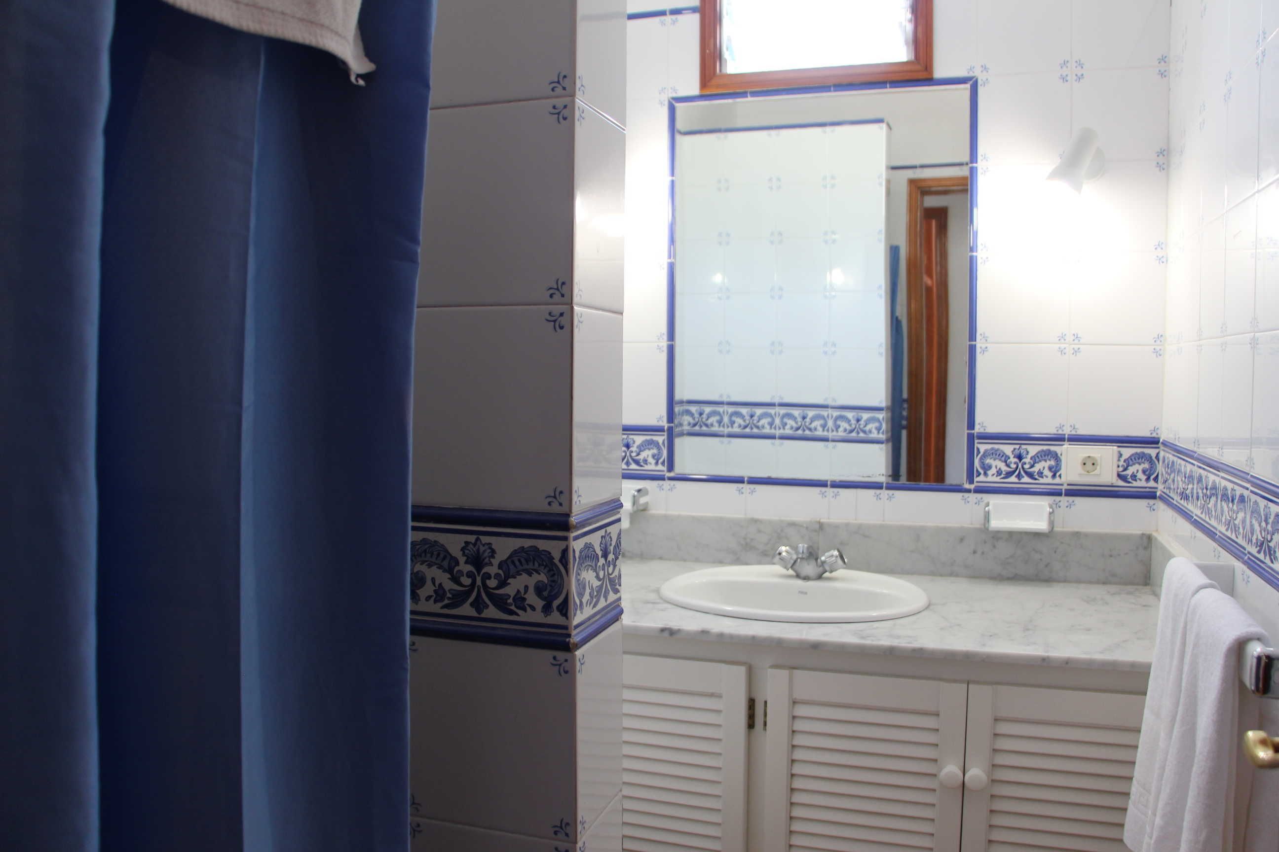 Un bagno con un lavandino bianco, piastrelle a motivi blu e bianchi, uno specchio e una finestra.