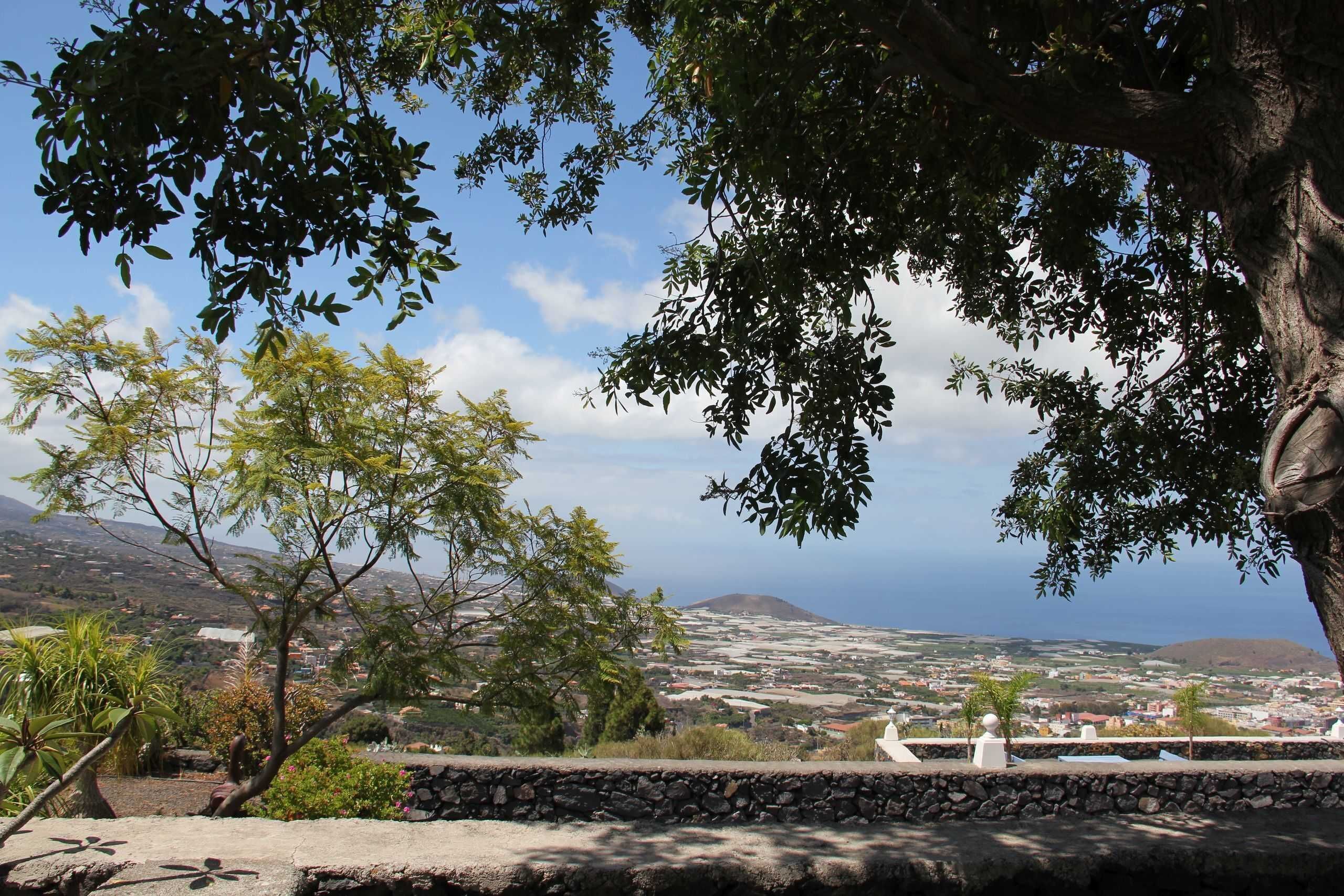 Un mur de pierre offrant une vue sur une ville côtière et une montagne à l’horizon.