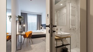 Una camera d'albergo moderna con un letto, una scrivania, una sedia e un bagno con lavandino e specchio.