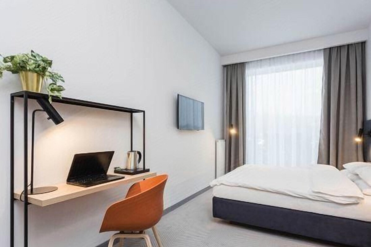 Une chambre d’hôtel avec un lit, un bureau avec un ordinateur portable, une chaise et une plante.