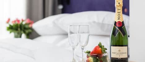 A bottle of Moët & Chandon Imperial Brut champagne, two empty glasses, and a small glass with strawberries on a bedside table in a hotel room.