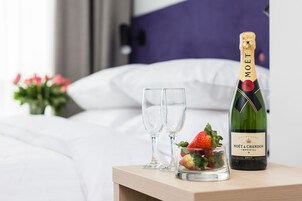 Une bouteille de champagne Moët & Chandon Imperial Brut, deux verres vides et un petit verre contenant des fraises, sur une table de chevet dans une chambre d’hôtel.