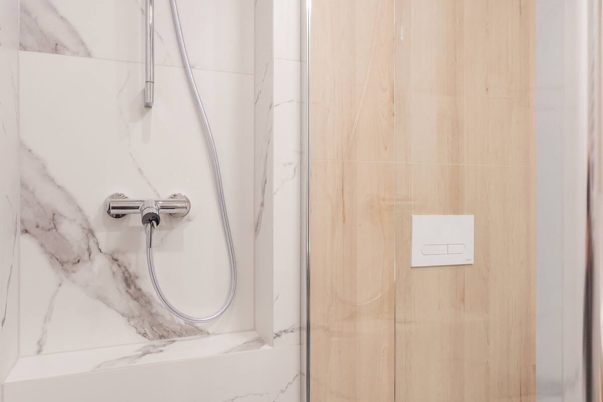 Une salle de bain moderne avec un mur de douche en marbre, des toilettes et une cabine de douche en verre.