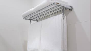 A white towel hanging on a chrome towel rack in a bathroom with white tiled walls.