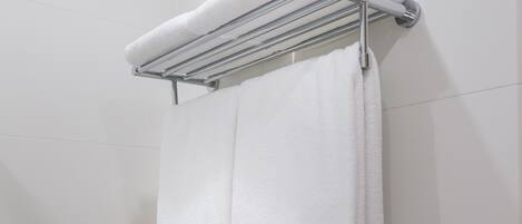 A white towel hanging on a chrome towel rack in a bathroom with white tiled walls.