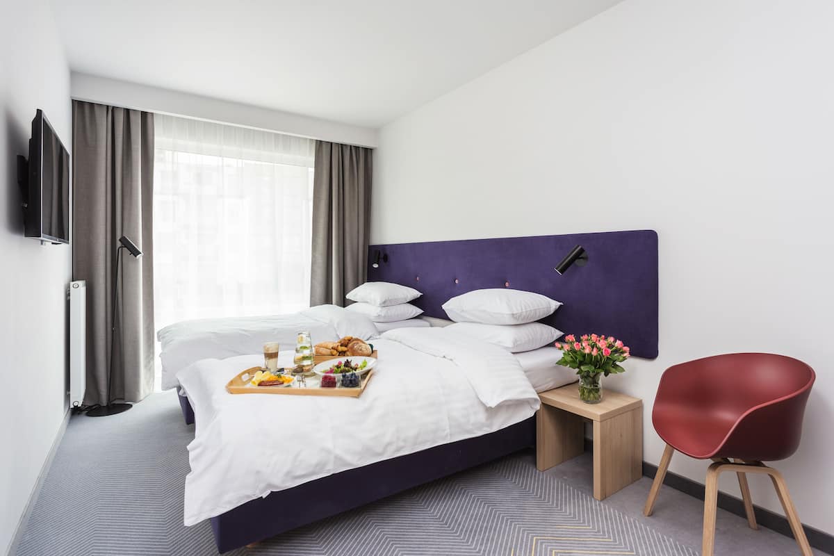 Une chambre d’hôtel avec un grand lit, une télévision, un plateau de petit-déjeuner, un vase de fleurs et un fauteuil rouge.