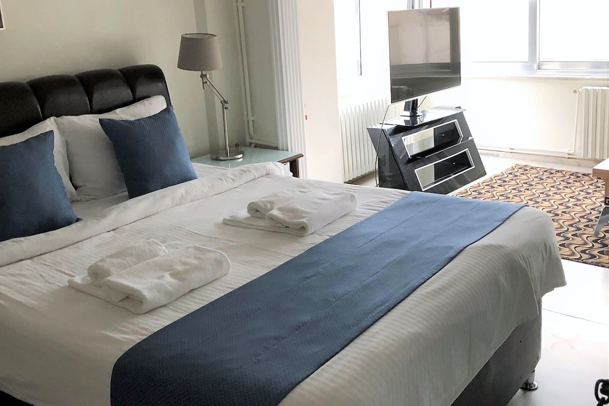 A neatly made bed with blue and white bedding, a bedside lamp, and a TV on a stand.