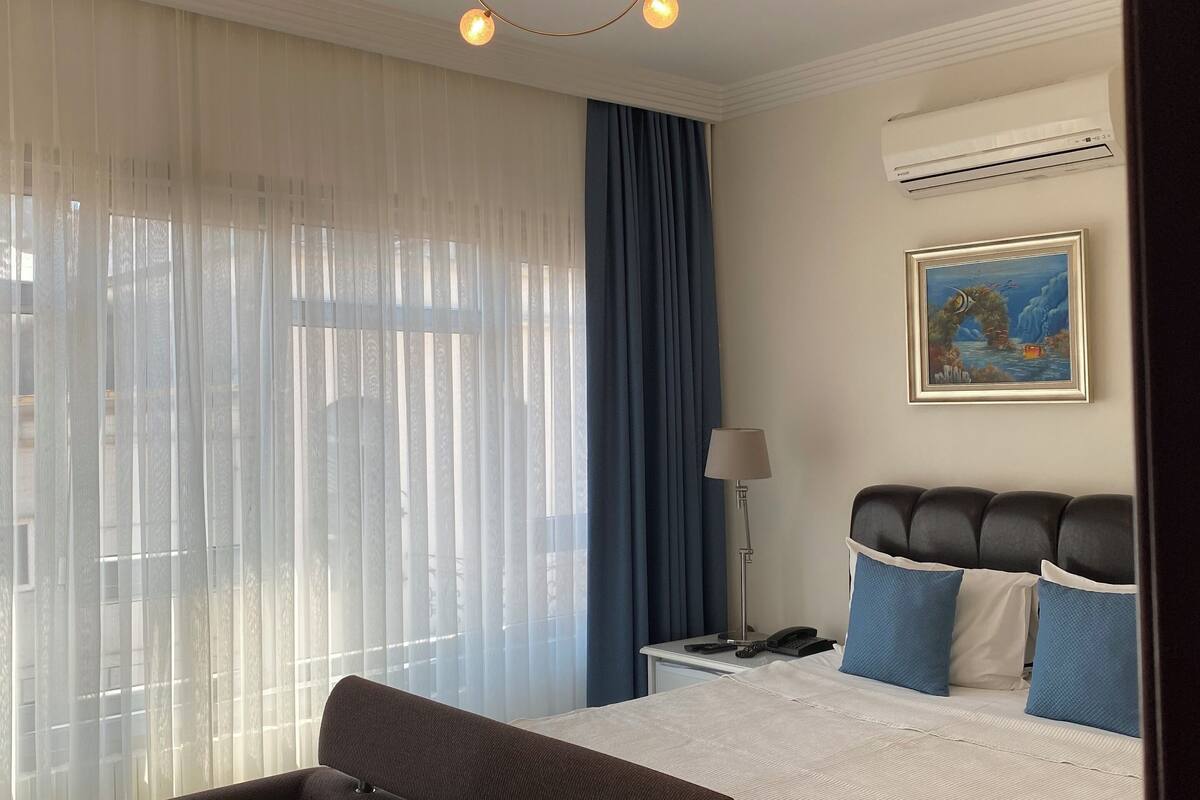 A hotel room with a bed, a desk, a chair, and a ceiling light fixture.