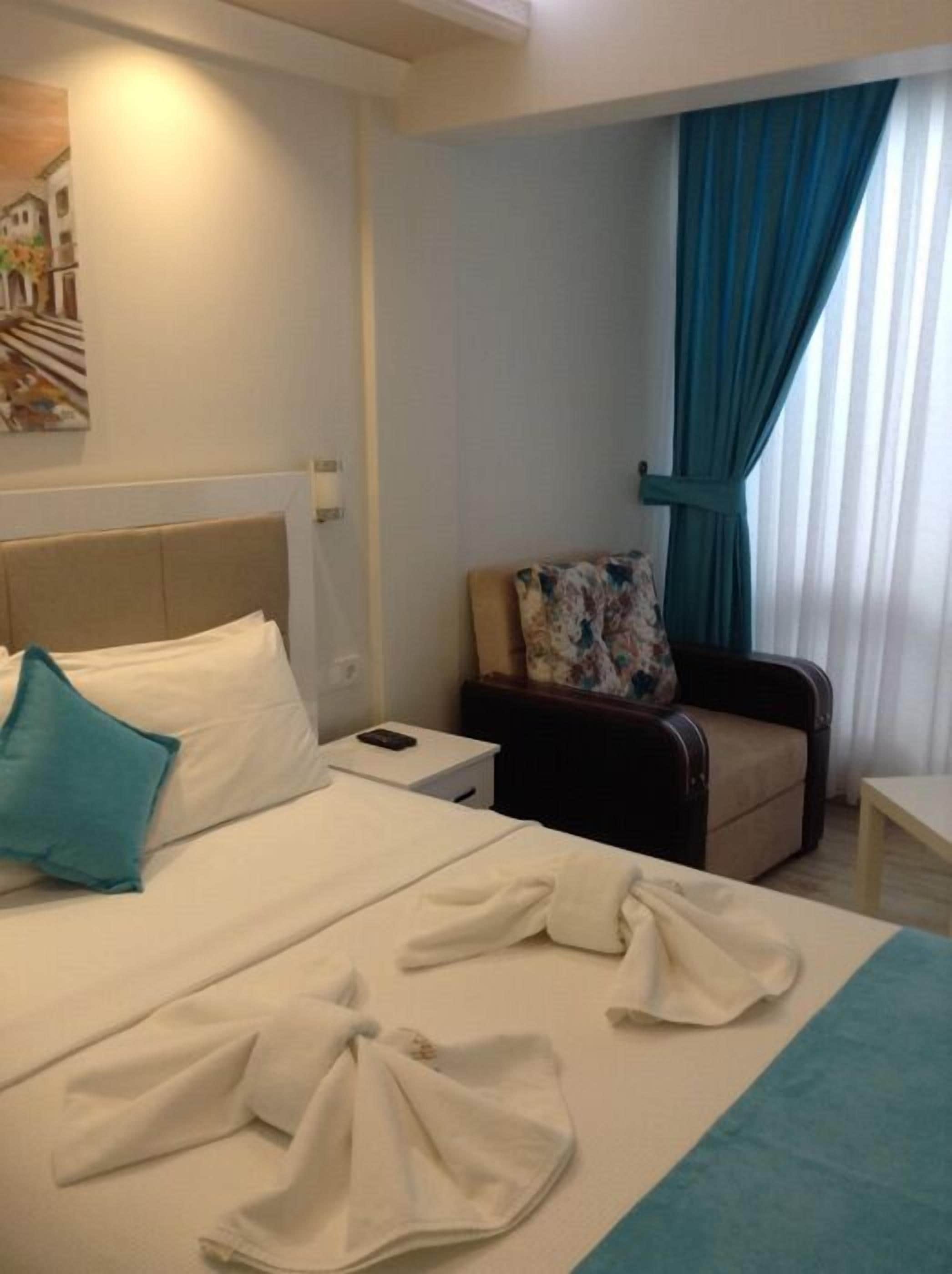 A hotel room with a bed, a chair, a nightstand, and a window with curtains.