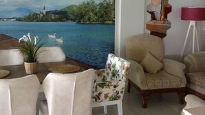 Un comedor con un gran mural de un lago y montañas, una araña y un espejo hexagonal en la pared.