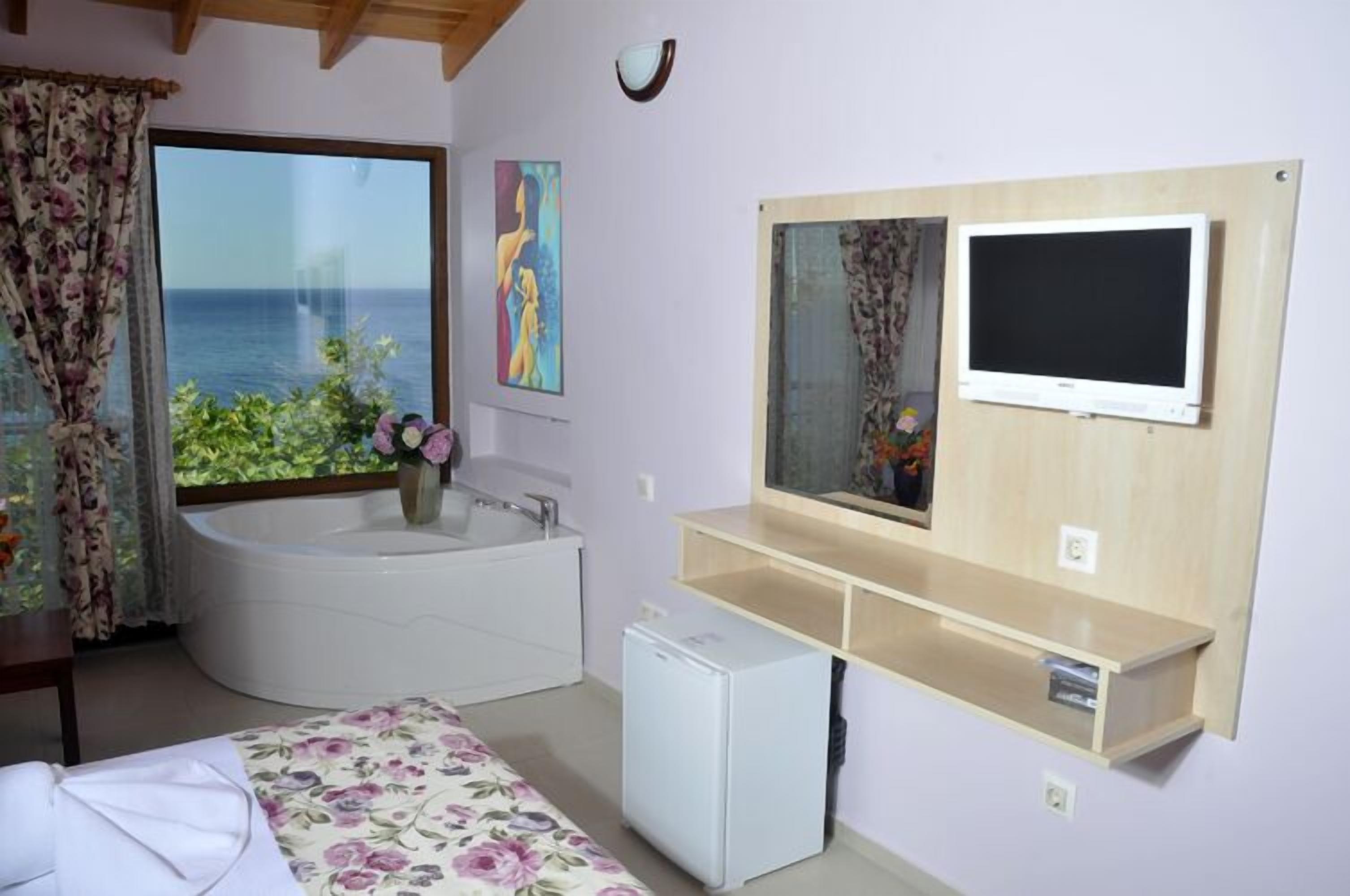 Un dormitorio con un ventanal grande, una bañera, un televisor y un refrigerador pequeño.