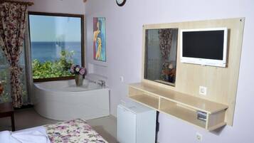 Un dormitorio con un ventanal grande, una bañera, un televisor y un refrigerador pequeño.