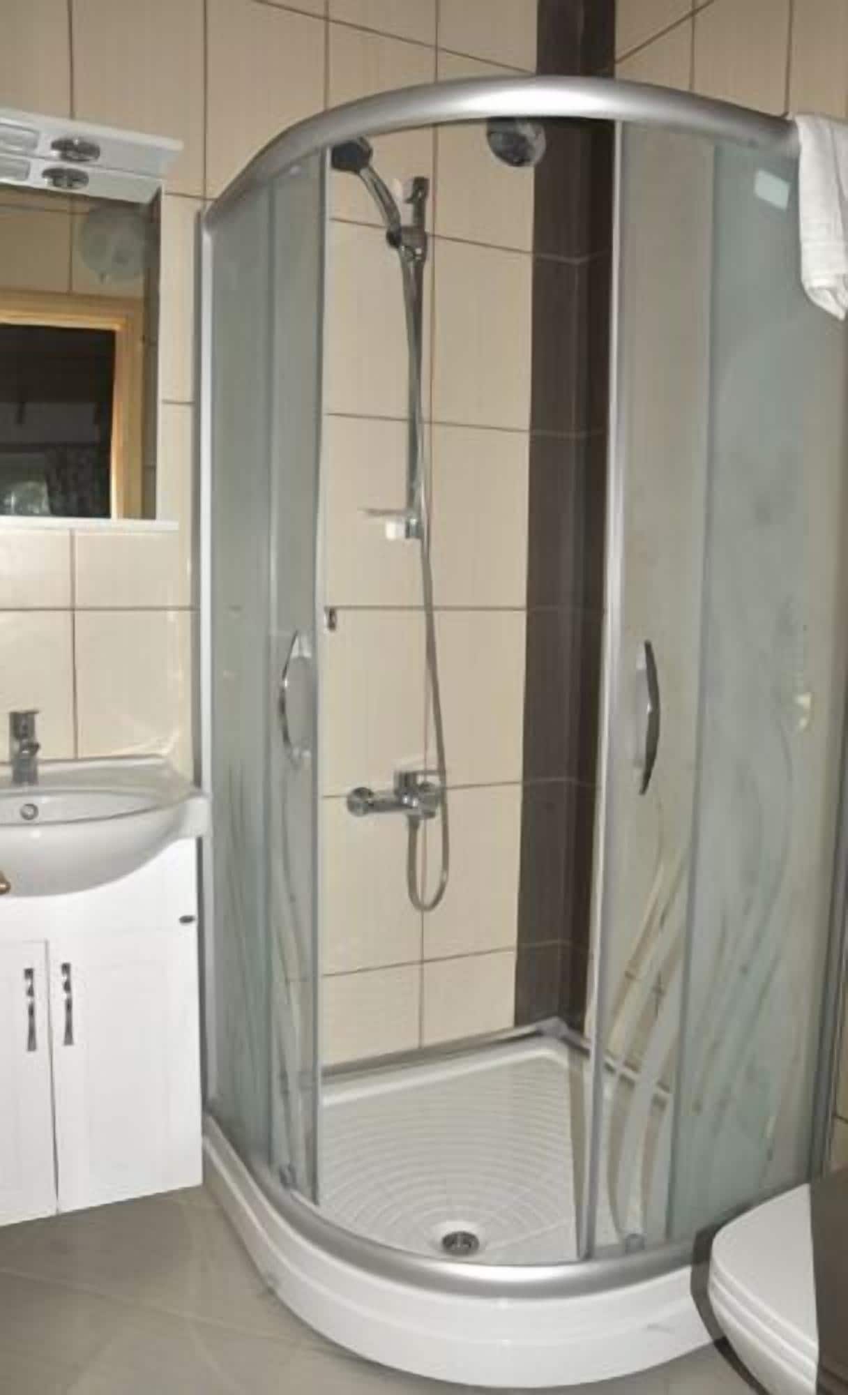 Een badkamer met een douche met glazen wand, een wastafel en kastjes.