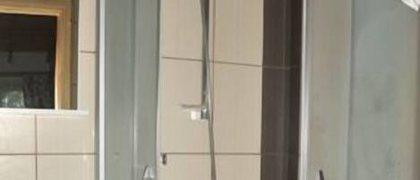 Een badkamer met een douche met glazen wand, een wastafel en kastjes.