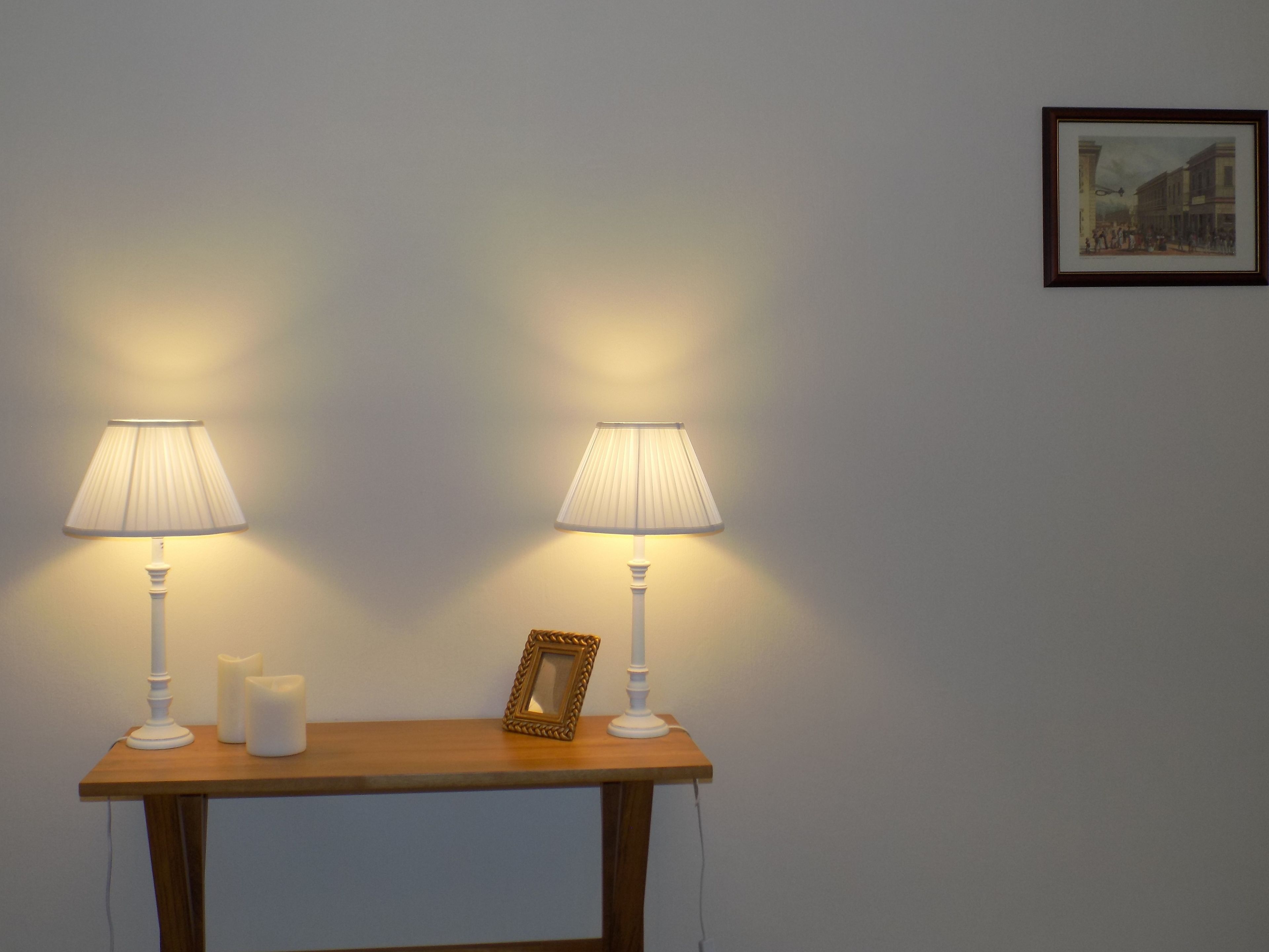 A table with two white lamps, two candles, and a framed picture.
