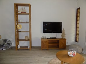 A living room with a wooden bookshelf, a television, a small Christmas tree, a fan, and a round table with a glass bowl. - The Beach Retreat (Cap Malheureux)