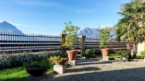A garden with potted plants and a gravel path, a metal fence, and a mountain in the background. - Villa La Rossa (Varenna)
