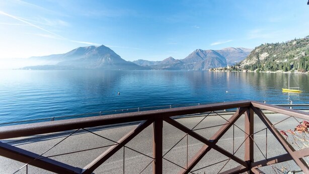 A lake with mountains in the background, a clear sky, and a metal railing in the foreground. - Villa La Rossa (Varenna)