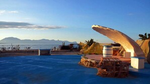 Un espace aménagé au bord de la piscine, avec une terrasse en bois, une grande sculpture en bois et une vue sur la mer et les montagnes en arrière-plan.