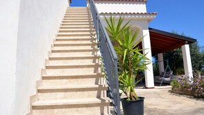 Un escalier menant à un bâtiment doté d’un toit recouvert de tuiles rouges, d’un patio abrité et d’une plante en pot.
