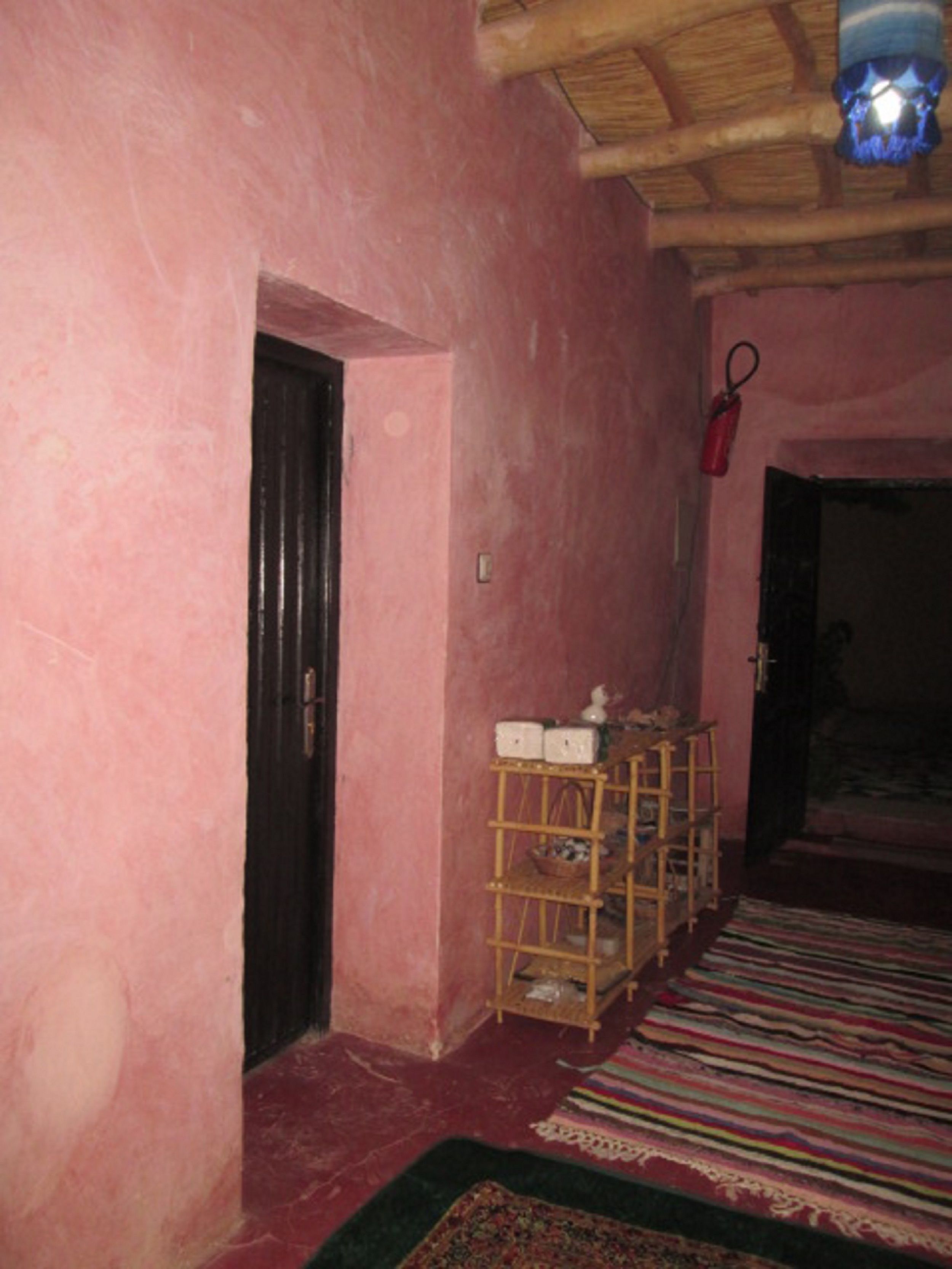 A room with pink walls, a wooden door, a shelf with items, and a patterned rug.