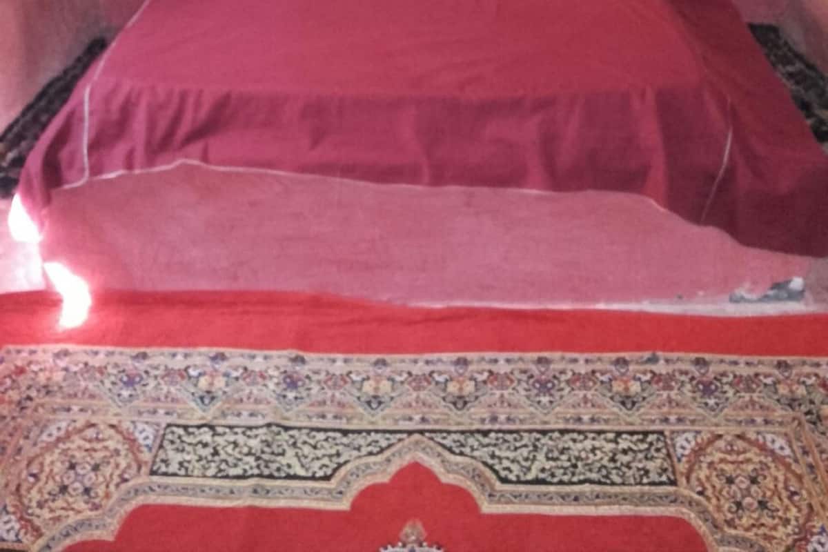Un lit avec une couvre-lit rouge et deux oreillers, un tapis à motifs et un mur uni.