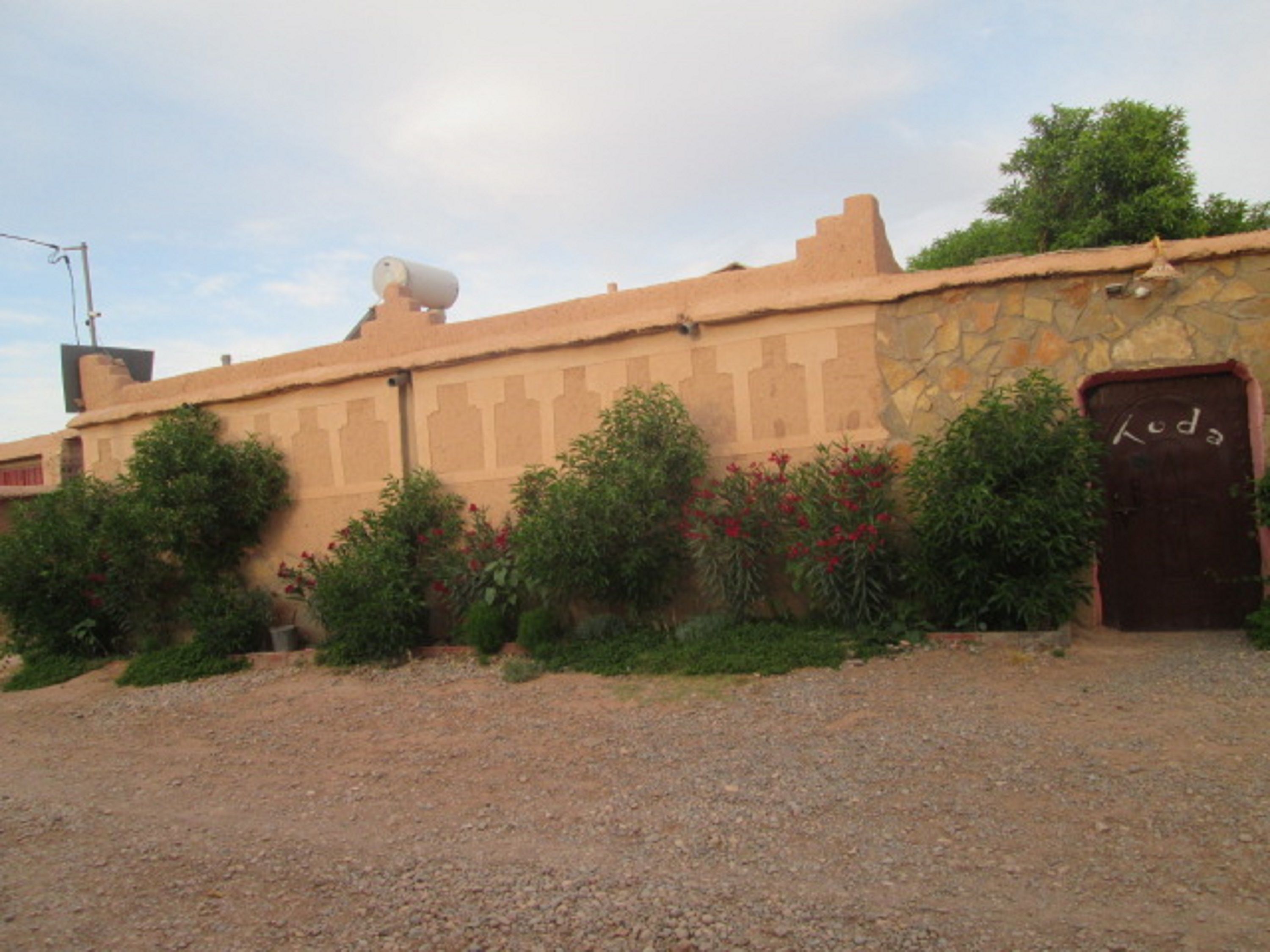 A building with a stone facade, a door labeled "Koda," and a surveillance camera on the roof.