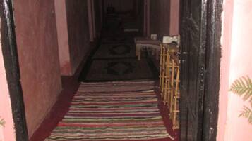 A narrow hallway with a red carpet leading to a door, wooden furniture, and a patterned rug.