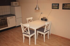 Cozinha compacta com micro-ondas, fogão e geladeira. Há uma mesa de jantar com quatro cadeiras e um rádio.