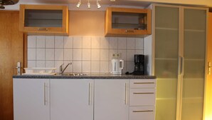A kitchen with white cabinets, a granite countertop, a coffee maker, and a refrigerator. - Volker Callsen Ferienwohnungen - Holiday apartment Heimathafen (Gelting)
