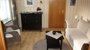 A furnished living room with a sofa, a small table with a vase, a dresser, and a door. - Volker Callsen Ferienwohnungen - Holiday apartment Heimathafen (Gelting)