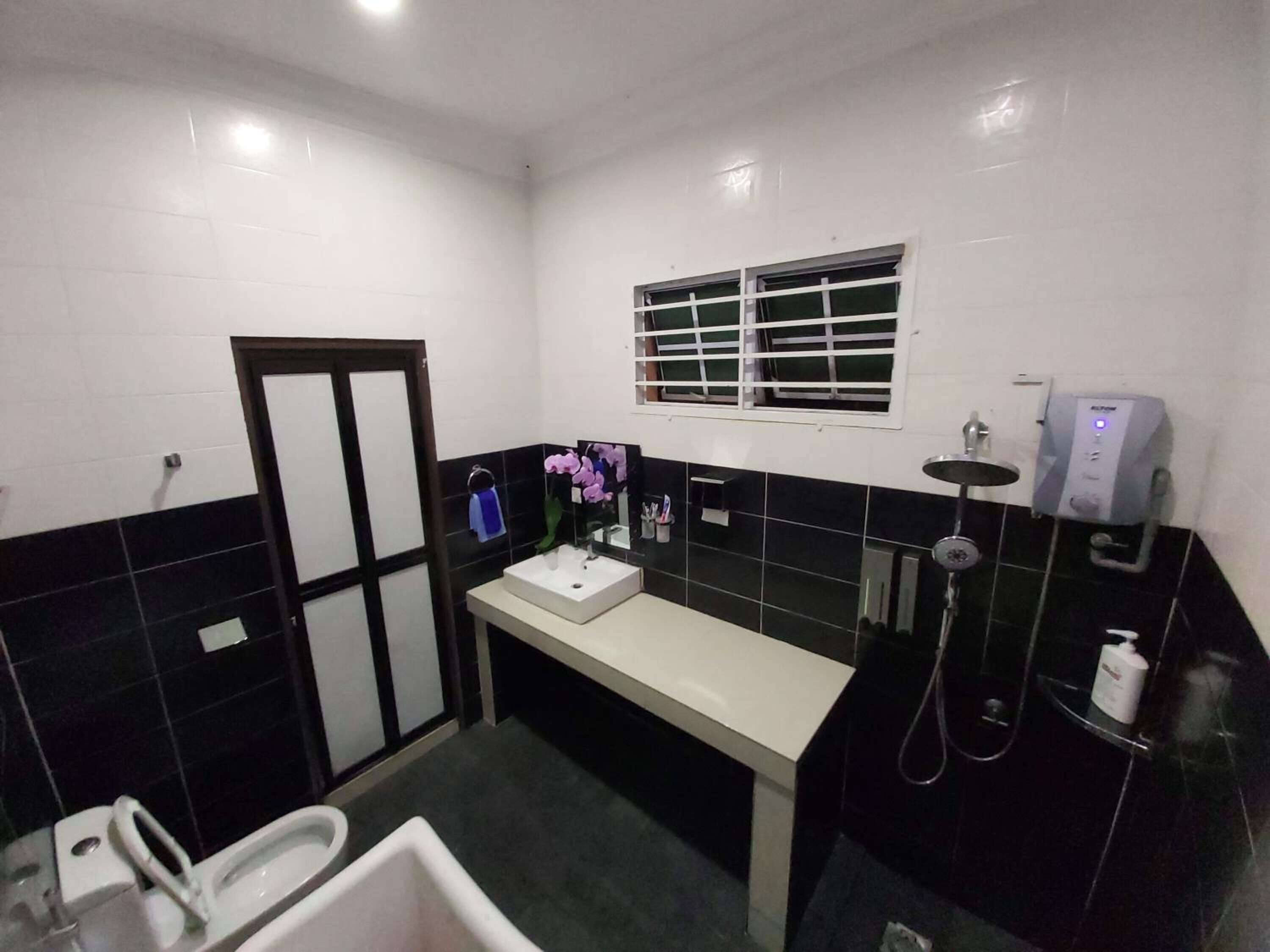 A bathroom with a white sink, black and white tiled walls, a window with bars, a handheld showerhead, and a toilet.