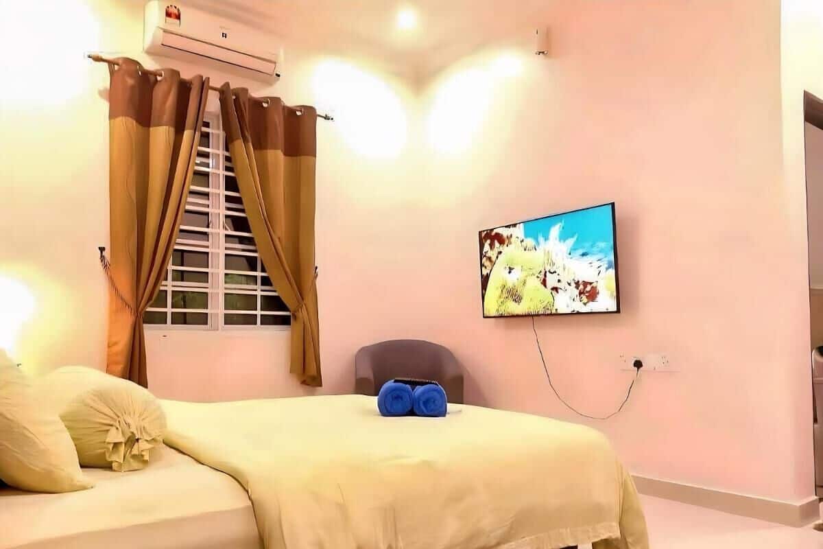 A hotel room with a bed, a window with curtains, an air conditioner, a wall-mounted TV, and a power outlet.