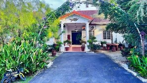 Una villa con entrada empedrada, rodeada de exuberante vegetación y macetas.