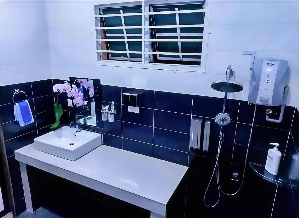 A modern bathroom with a white sink, black tiles, a window with blinds, a handheld showerhead, and a soap dispenser.