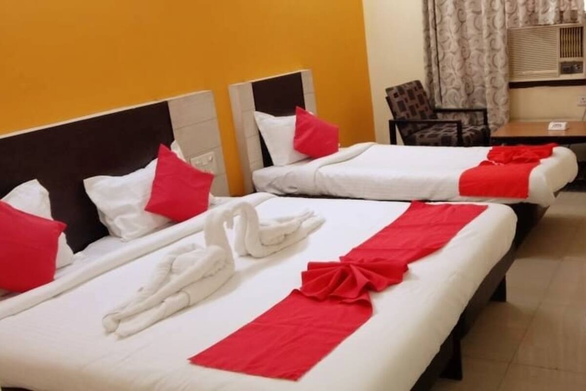 A hotel room with two beds, each with white linens and red accents, a wooden table, and patterned curtains.