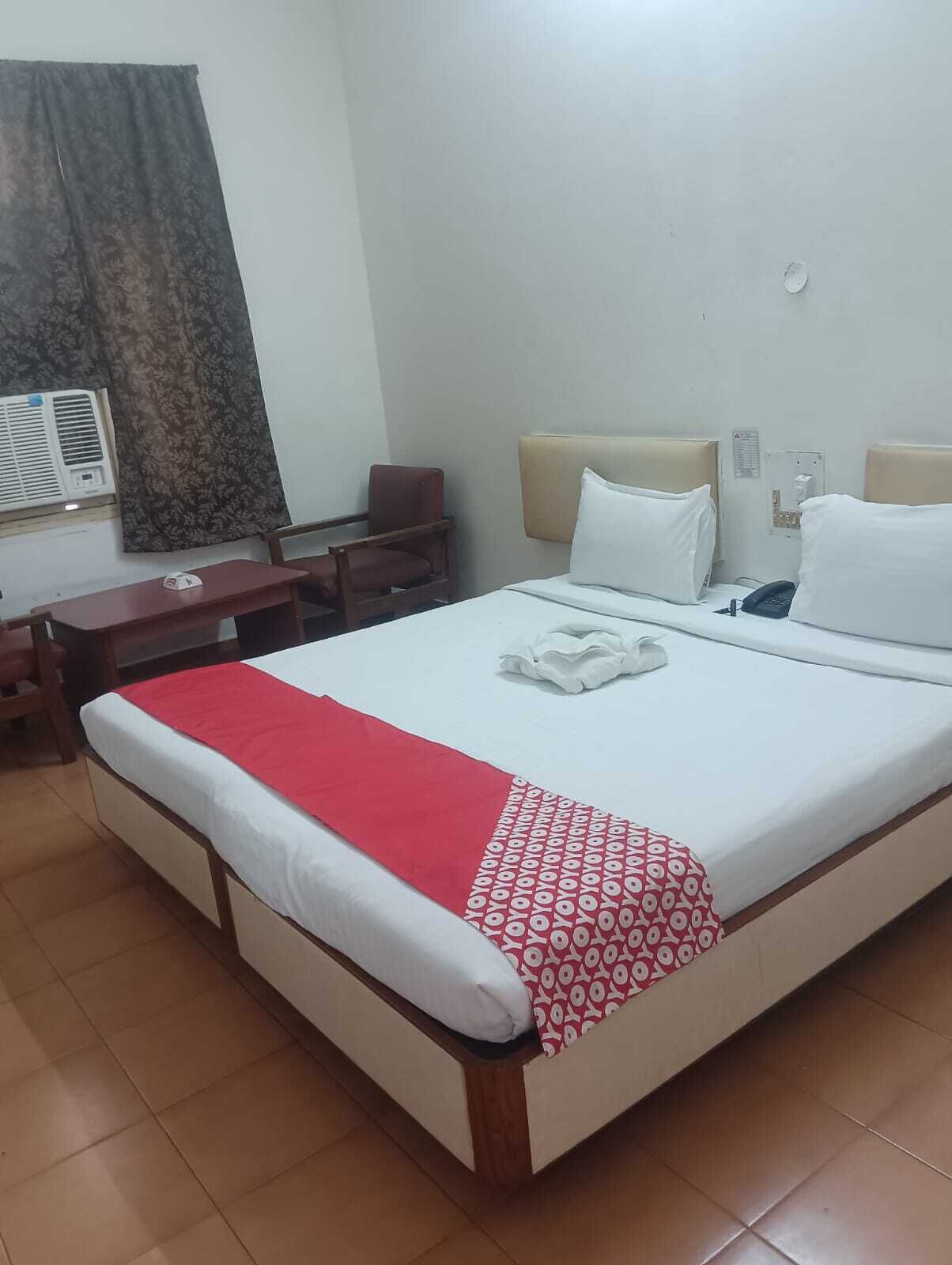 A hotel room with a large bed, a desk, a chair, and a wall-mounted air conditioning unit.